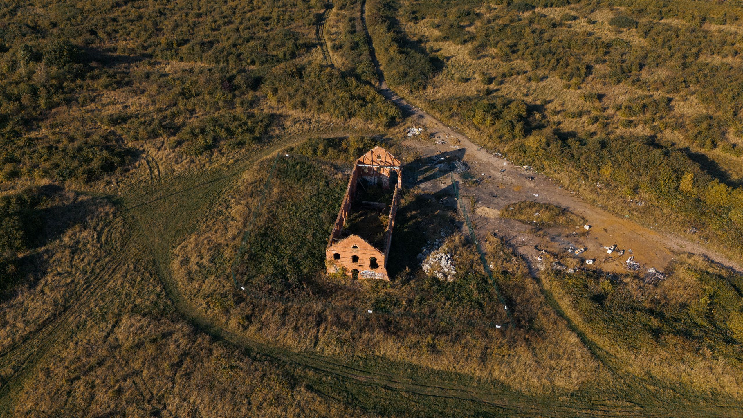 Aerial photograph of a roofless red-brick building in an overgrown landscape