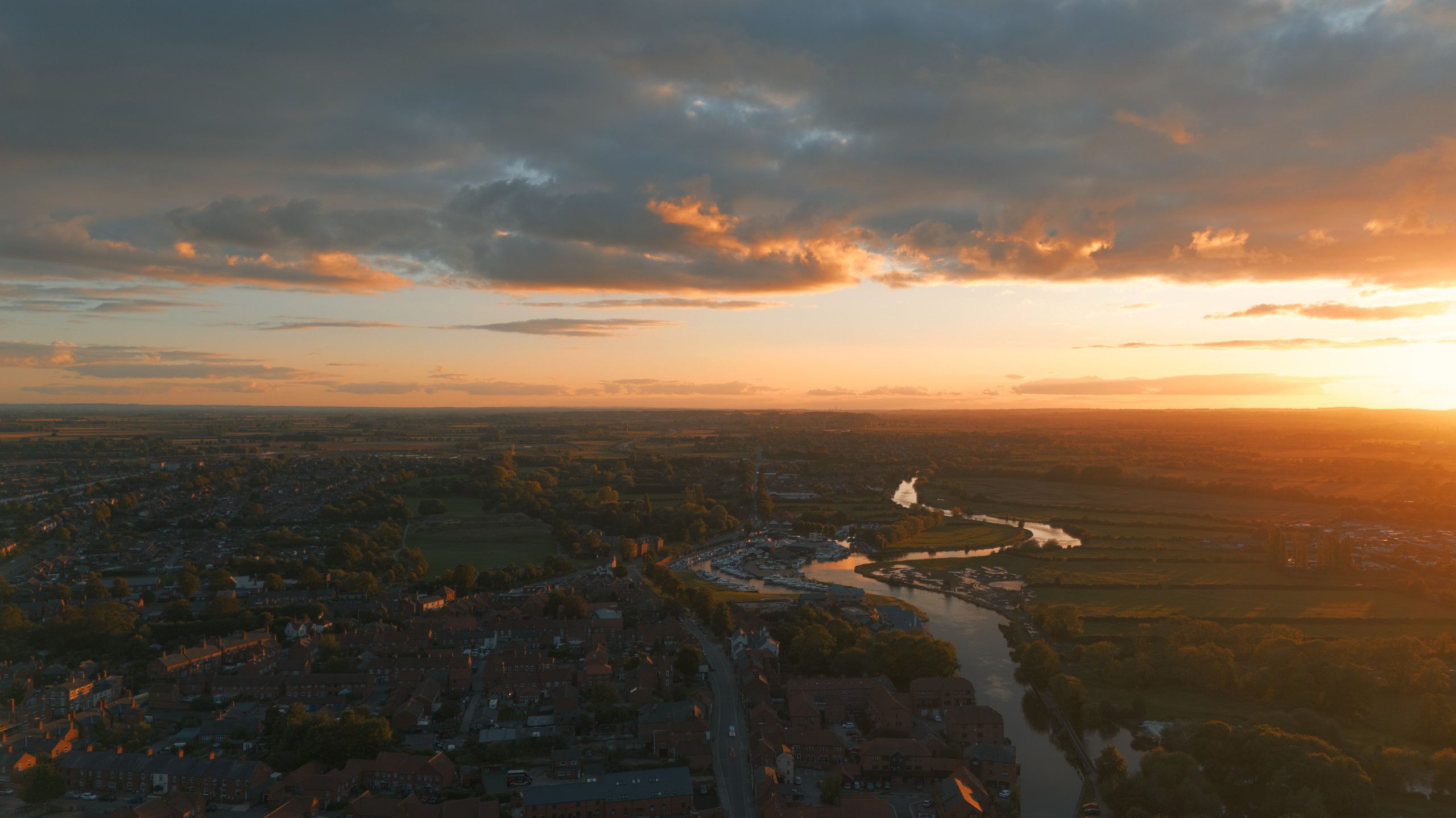 Aerial view of a winding river, rooftops and fields beneath an orange sunset